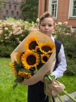 Подросток с букетом подсолнечников на улице возле цветущего сада.