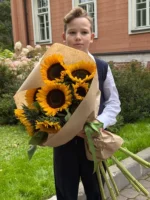 Яркие подсолнухи в руках ребенка, праздничный букет на улице.