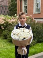 Цветы в руках школьника на фоне цветущего сада и старинного здания, символ праздника и внимания.