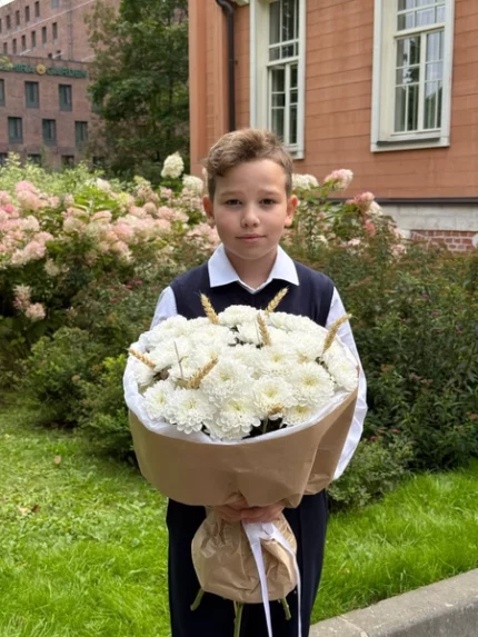 Цветы в руках школьника на фоне цветущего сада и старинного здания, символ праздника и внимания.