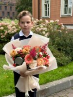 Яркое изображение мальчика с букетом цветов на фоне зеленого сада и жилого здания, символизирующее особый случай или поздравление.