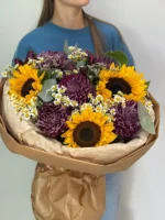 Яркий букет из солнечных подсолнухов и осенних хризантем с ромашками, подаренный женщине.