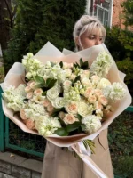 Роскошный букет из белых и бежевых роз с зеленью, девушка с цветами на улице.