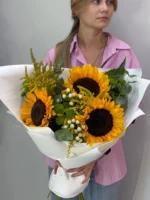 Яркий букет подсолнухов и зеленых растений, подаренный женщине.